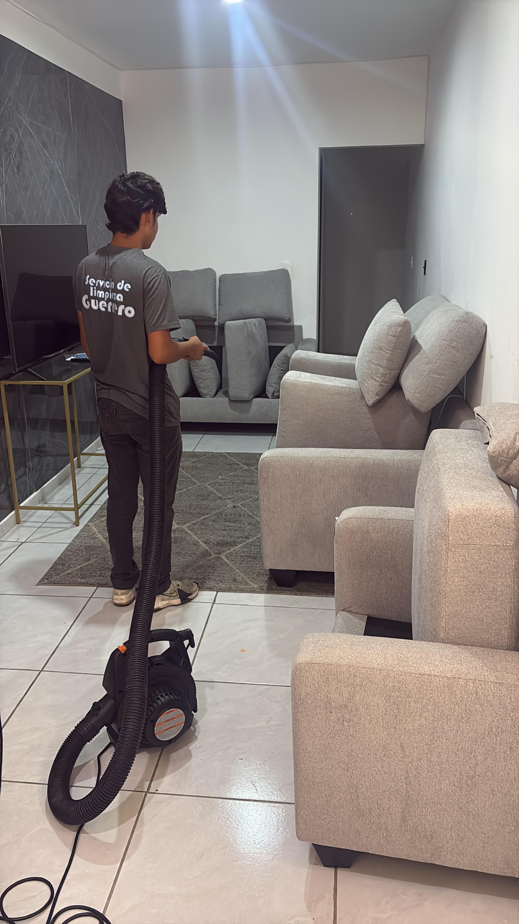 Persona aspirando un sillón gris en una sala moderna.